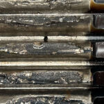 Close-up of a stack of worn, serrated metal blades with rust and grime visible on rough surfaces (macro shot).
