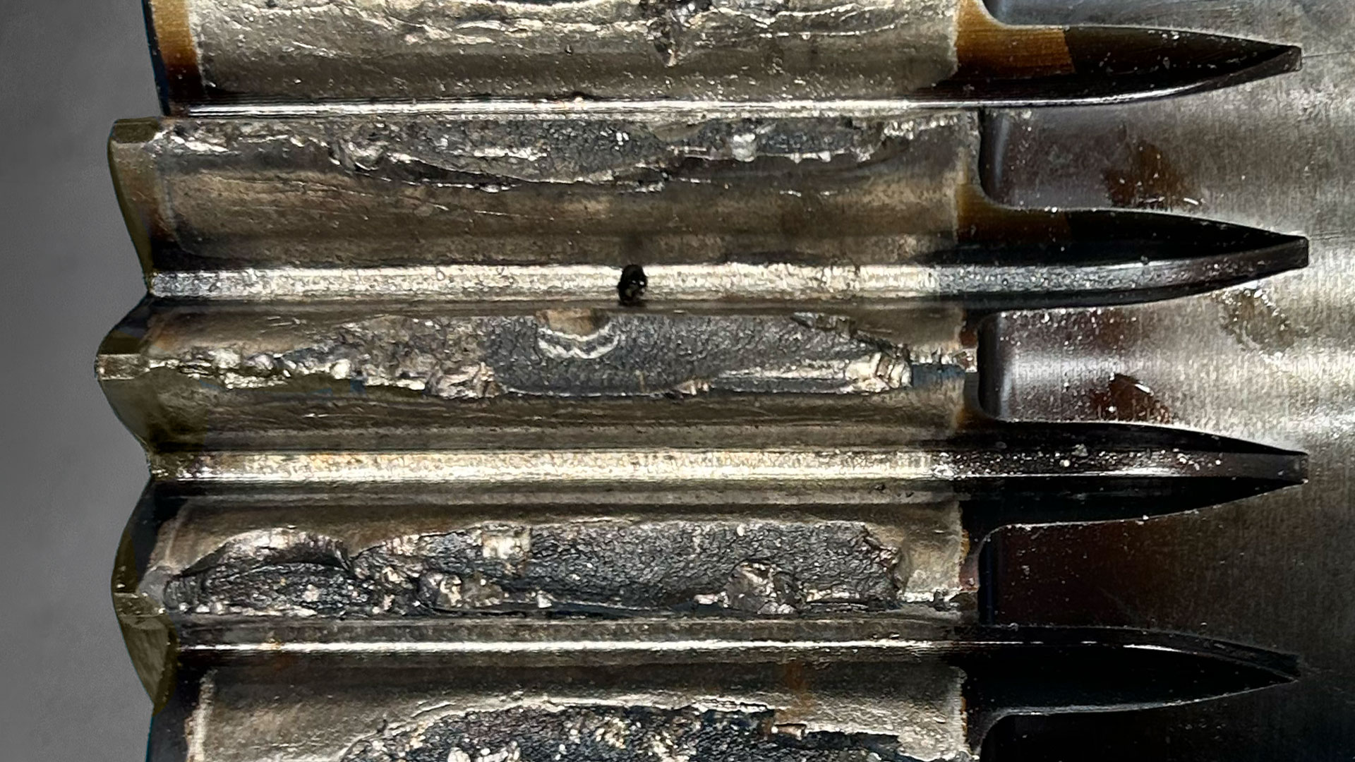 Close-up of a stack of worn, serrated metal blades with rust and grime visible on rough surfaces (macro shot).